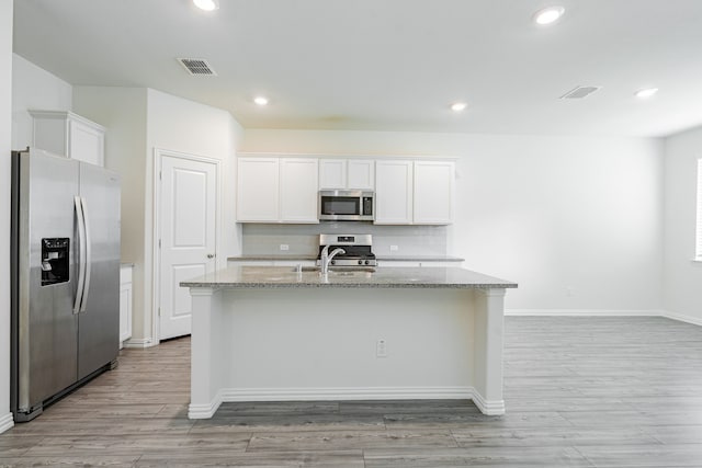624 Beltrand Ln, Fate, TX 75087 - kitchen with stainless steel appliances, light stone countertops, white cabinetry, a center island with sink, and light wood finished floors