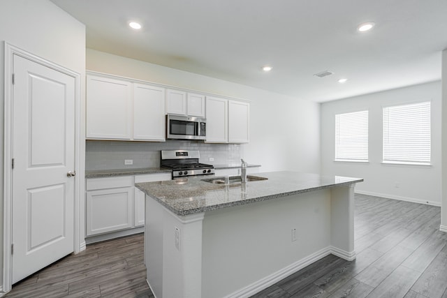 624 Beltrand Ln, Fate, TX 75087 - kitchen featuring stainless steel appliances, light stone counters, decorative backsplash, dark wood-style floors, and a kitchen island with sink