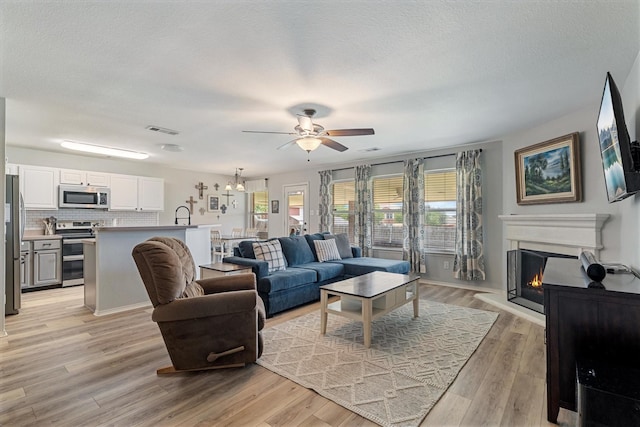 1036 Ridgetop Dr, Justin, TX 76247 - living area with ceiling fan, light wood-style floors, a lit fireplace, a textured ceiling, and a chandelier
