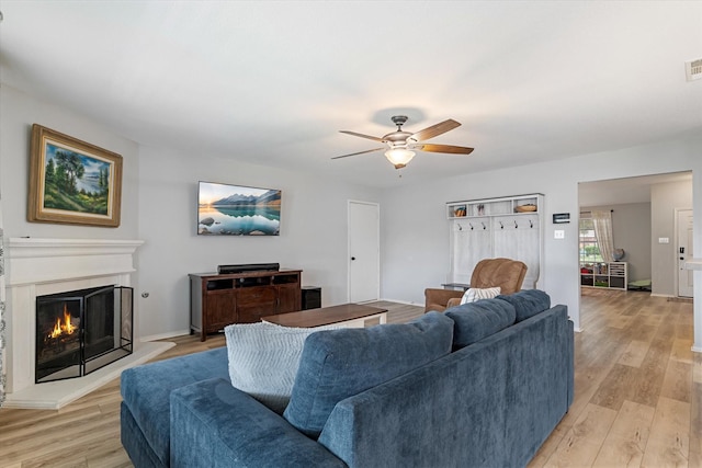 1036 Ridgetop Dr, Justin, TX 76247 - living room with ceiling fan, a warm lit fireplace, and light wood-style floors