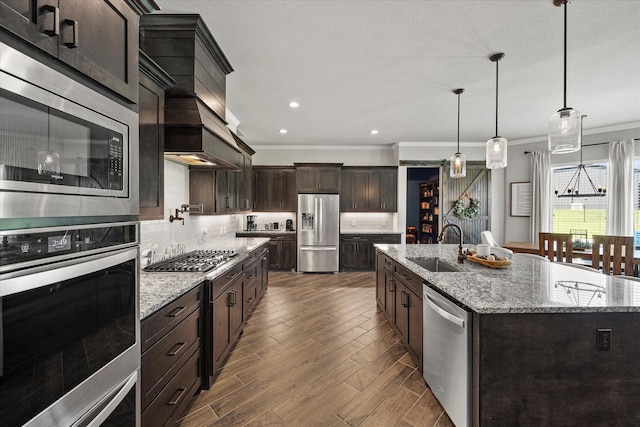 1007 Sinopa St, Caddo Mills, TX 75135 - kitchen featuring appliances with stainless steel finishes, ornamental molding, a large island with sink, dark brown cabinets, and backsplash