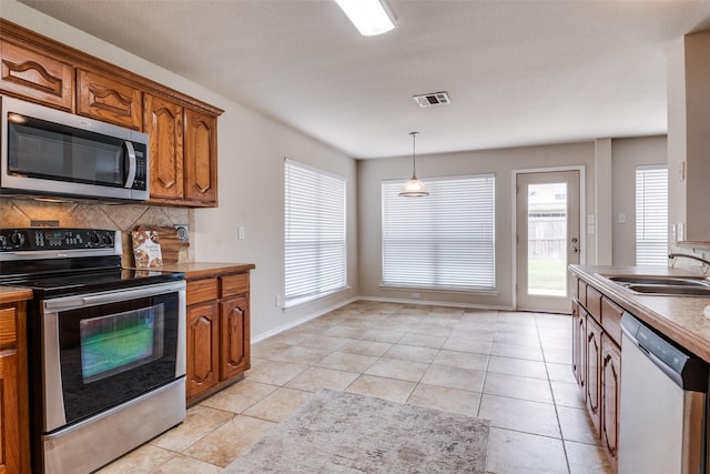 2600 Spencer Cir, Royse City, TX 75189 - kitchen with appliances with stainless steel finishes, a sink, brown cabinets, light tile patterned flooring, and decorative light fixtures