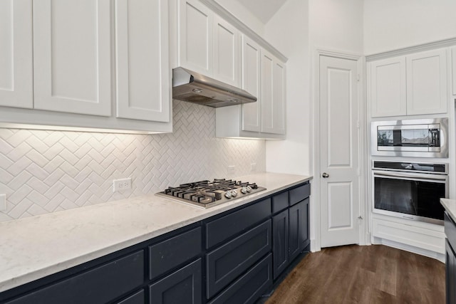2208 13th St, Argyle, TX 76226 - kitchen with appliances with stainless steel finishes, under cabinet range hood, white cabinets, tasteful backsplash, and dark wood-type flooring