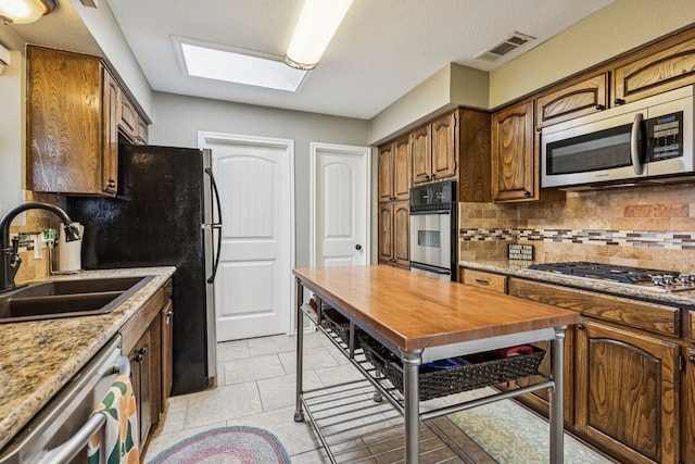 4008 Lynbrook Ln, Arlington, TX 76015 - kitchen with appliances with stainless steel finishes, a sink, decorative backsplash, a skylight, and light tile patterned floors