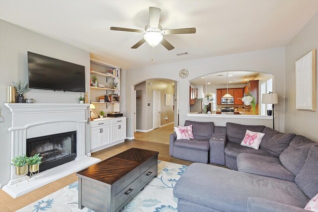 7009 Bishop Pine Rd, Denton, TX 76208 - living room featuring a ceiling fan, arched walkways, light wood-type flooring, and a fireplace with raised hearth