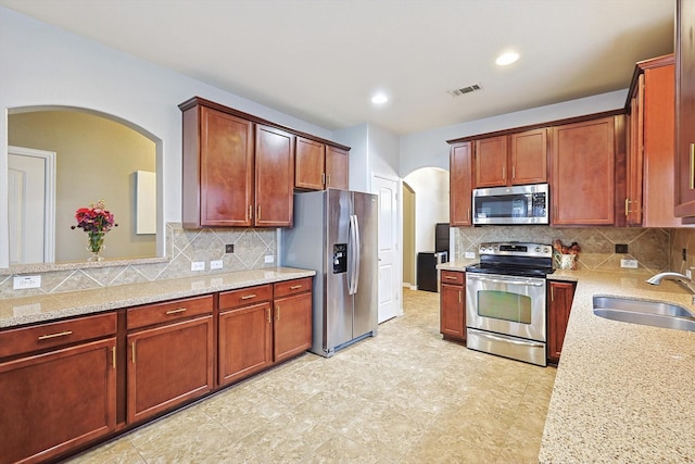 7009 Bishop Pine Rd, Denton, TX 76208 - kitchen with stainless steel appliances, a sink, arched walkways, decorative backsplash, and light stone countertops
