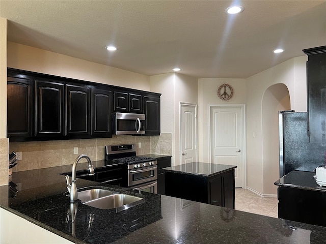 5420 Chinkapin Ln, Fort Worth, TX 76244 - kitchen with stainless steel appliances, a sink, dark cabinets, arched walkways, and dark stone counters