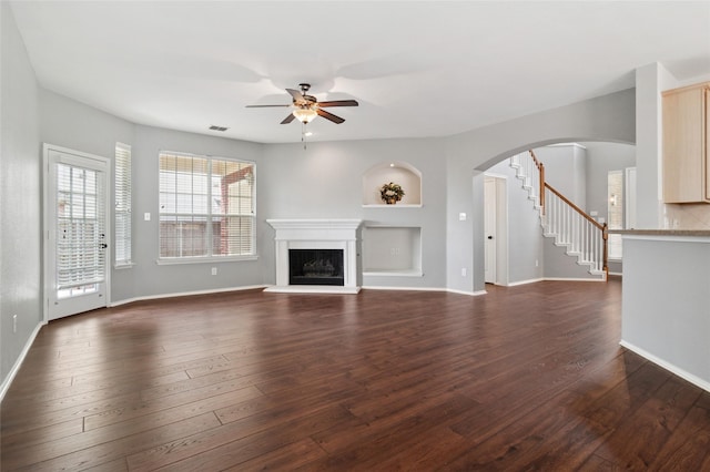 2125 Garden Crest Dr, Rockwall, TX 75087 - unfurnished living room featuring a ceiling fan, arched walkways, stairs, a fireplace with raised hearth, and dark wood-style floors