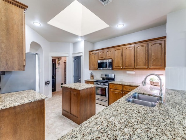 3033 Maple Creek Dr, Fort Worth, TX 76177 - kitchen featuring appliances with stainless steel finishes, a sink, light stone counters, arched walkways, and brown cabinets
