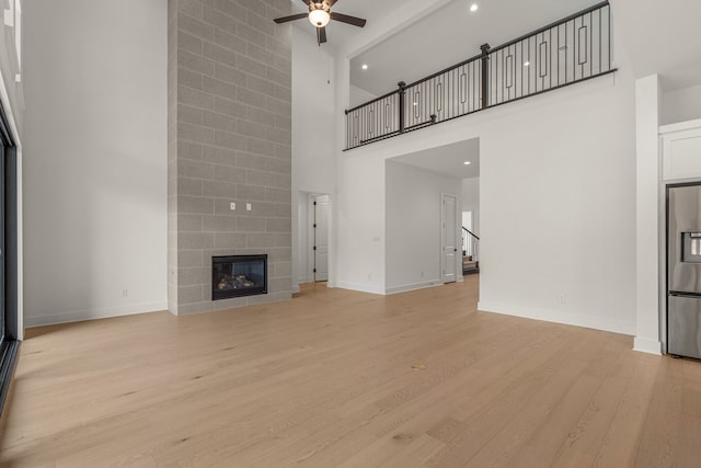 14085 Nicollet Dr, Frisco, TX 75033 - unfurnished living room featuring a high ceiling, a ceiling fan, light wood-style floors, baseboards, and a tile fireplace