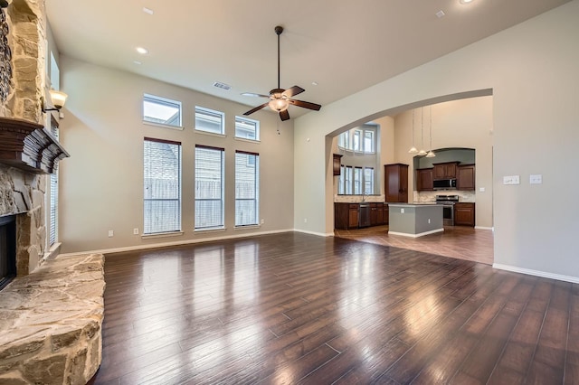 9028 Wiggins Dr, Fort Worth, TX 76244 - unfurnished living room featuring a stone fireplace, dark wood-style floors, ceiling fan, arched walkways, and a high ceiling
