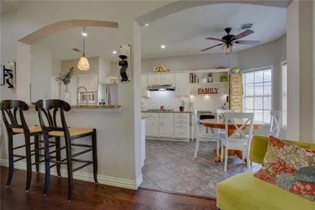 14 E Hillside Pl, Trophy Club, TX 76262 - kitchen with under cabinet range hood, arched walkways, a ceiling fan, tasteful backsplash, and a kitchen bar