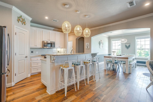 106 Camelot St, Glen Rose, TX 76043 - kitchen with stainless steel appliances, arched walkways, light wood-style flooring, a breakfast bar, and crown molding