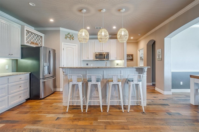 106 Camelot St, Glen Rose, TX 76043 - kitchen with stainless steel appliances, arched walkways, light wood finished floors, ornamental molding, and a kitchen bar