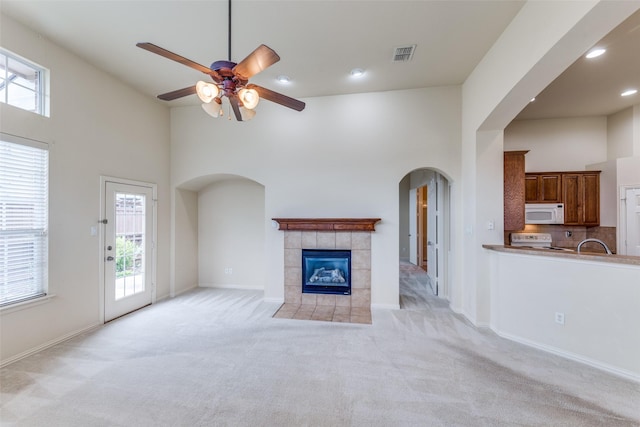 1728 Sandpiper Ln, Carrollton, TX 75007 - unfurnished living room with a towering ceiling, arched walkways, light carpet, a ceiling fan, and a tile fireplace