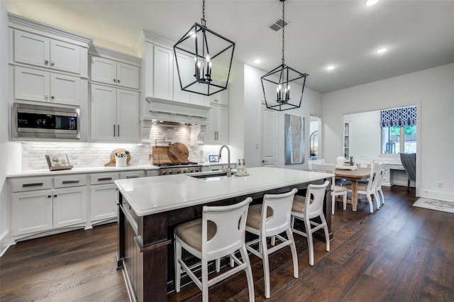 2021 Longmont Ln, Prosper, TX 75078 - kitchen featuring stainless steel microwave, a sink, light countertops, decorative backsplash, and a center island with sink