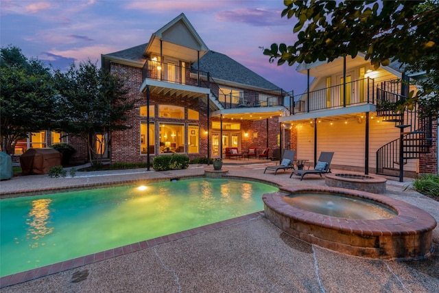 3873 Heritage Trl, Celina, TX 75009 - back of house at dusk featuring a balcony, stairway, a patio, brick siding, and a pool with connected hot tub