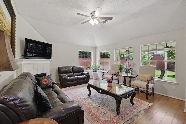 8217 Alderwood Pl, Plano, TX 75025 - living room featuring ceiling fan, lofted ceiling, a textured ceiling, a tile fireplace, and wood-type flooring