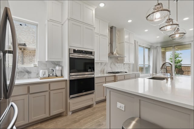 1001 Gentle Knoll Ln, Prosper, TX 75078 - kitchen featuring a sink, appliances with stainless steel finishes, wall chimney range hood, decorative backsplash, and light wood finished floors