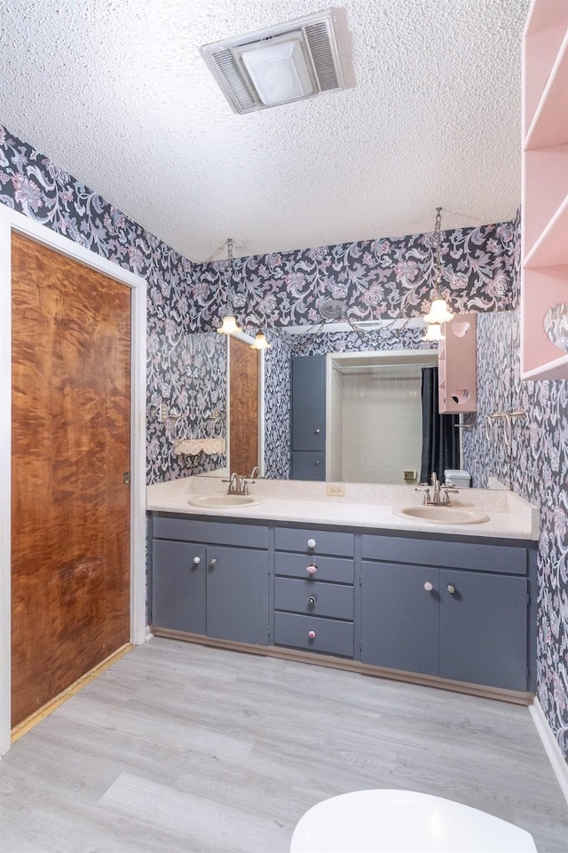 2992 County Road 100, Brady, TX 76825 - full bathroom with wallpapered walls, double vanity, wood finished floors, a textured ceiling, and baseboards