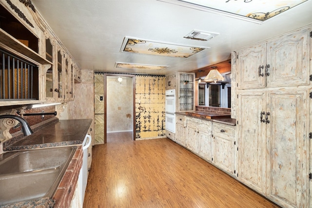 2992 County Road 100, Brady, TX 76825 - kitchen featuring a sink, dark countertops, double oven, light wood-type flooring, and glass insert cabinets