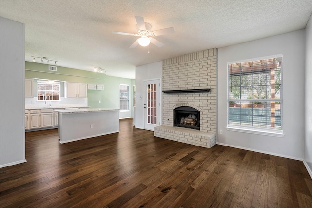 2221 Bennington Ave, Flower Mound, TX 75028 - unfurnished living room with a textured ceiling, dark wood-style flooring, ceiling fan, baseboards, and a sink