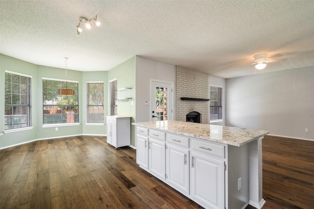 2221 Bennington Ave, Flower Mound, TX 75028 - kitchen with dark wood-type flooring, a fireplace, a textured ceiling, white cabinetry, and ceiling fan