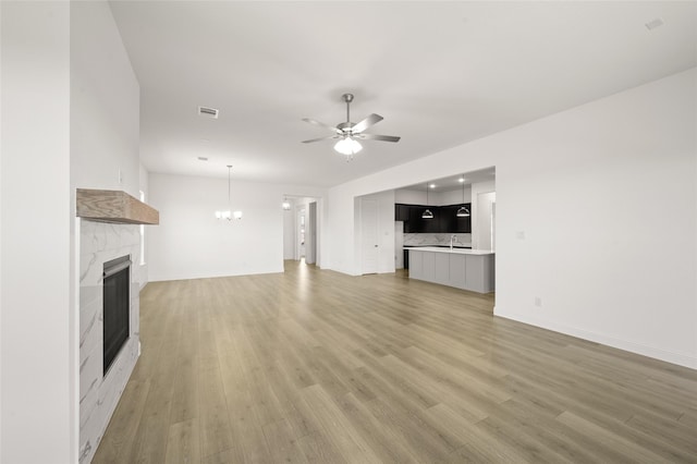 2397 Rams Horn Dr, Waxahachie, TX 75165 - unfurnished living room featuring a premium fireplace, ceiling fan, light wood finished floors, a chandelier, and baseboards