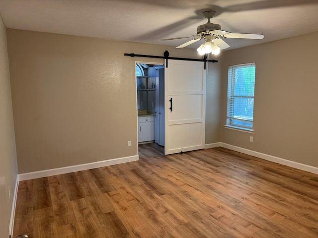 7750 Dentcrest Dr, Dallas, TX 75254 - unfurnished room featuring a barn door, wood finished floors, a ceiling fan, and baseboards