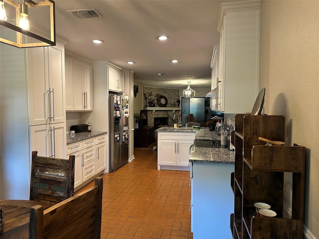7750 Dentcrest Dr, Dallas, TX 75254 - kitchen with a brick fireplace, brick patterned flooring, stainless steel fridge, white cabinetry, and recessed lighting