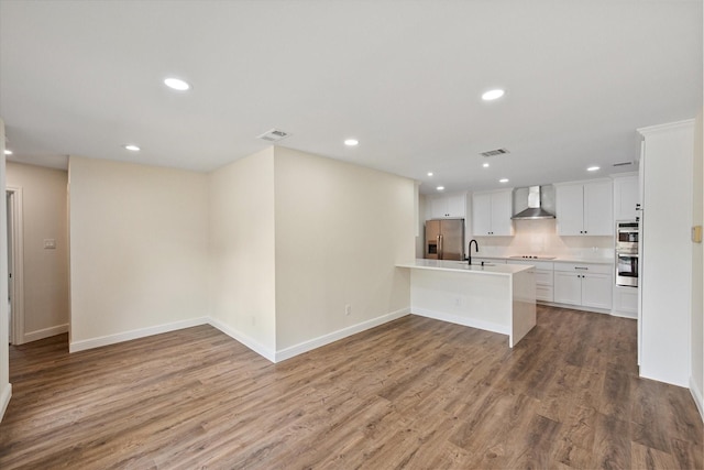 902 Mission Dr, Southlake, TX 76092 - kitchen featuring wall chimney range hood, stainless steel appliances, a sink, a peninsula, and wood finished floors