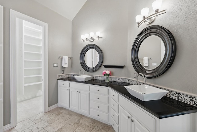 702 Malton Ln, Southlake, TX 76092 - bathroom featuring stone tile flooring, double vanity, a spacious closet, vaulted ceiling, and baseboards