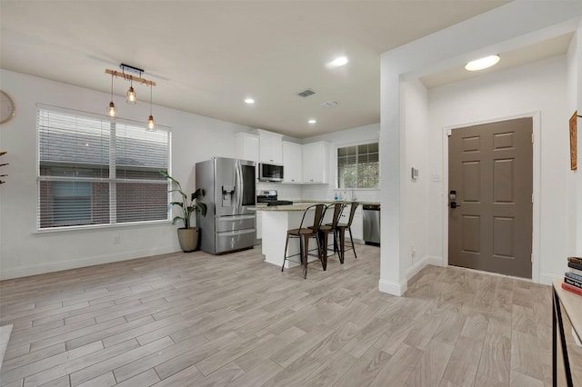 832 Lake Worth Trl, Little Elm, TX 75068 - kitchen featuring stainless steel appliances, a breakfast bar, white cabinetry, light wood-style floors, and a kitchen island