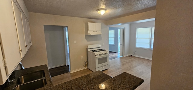 5170 Cardiff St, Dallas, TX 75241 - kitchen with white gas stove, wood finished floors, white cabinets, under cabinet range hood, and a textured ceiling