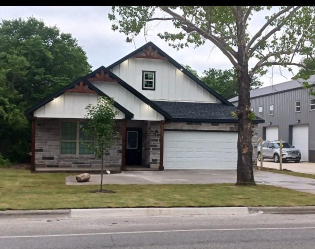 1118 S Grand Ave, Gainesville, TX 76240 - view of front facade featuring board and batten siding, driveway, a shingled roof, a front yard, and stone siding