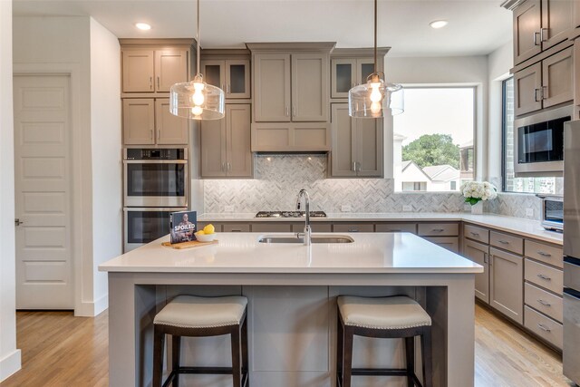 8120 Radnor Rd, Dallas, TX 75231 - kitchen with stainless steel appliances, backsplash, a kitchen breakfast bar, light wood-style flooring, and light countertops