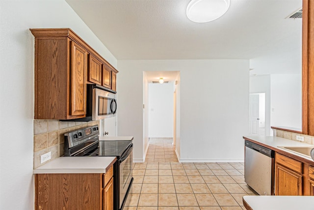 1301 Hennessey Ct, Fort Worth, TX 76131 - kitchen featuring stainless steel appliances, brown cabinets, decorative backsplash, and light tile patterned flooring