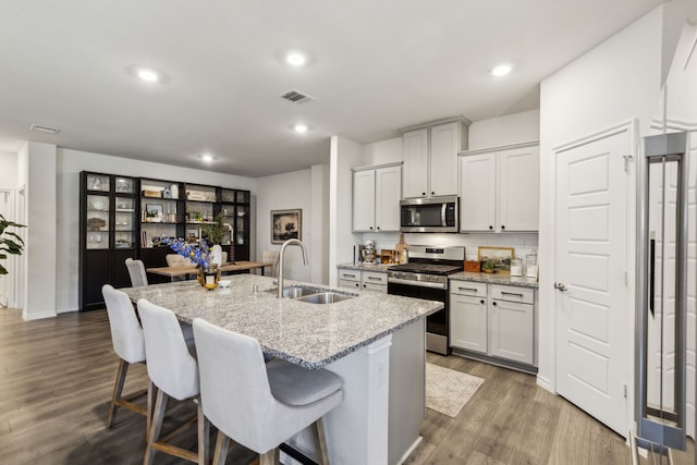 1104 Egret Way, Celina, TX 75009 - kitchen with appliances with stainless steel finishes, a sink, a kitchen breakfast bar, wood finished floors, and a kitchen island with sink