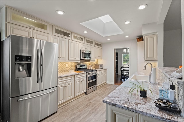 10420 Carry Back Cir, Dallas, TX 75229 - kitchen with stainless steel appliances, a skylight, decorative backsplash, light stone counters, and light wood-style floors