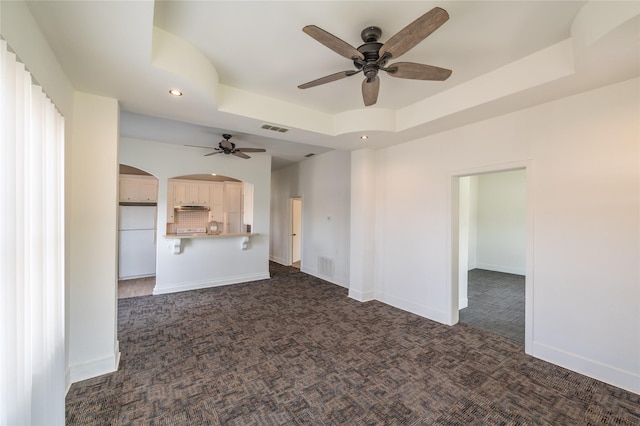101 S Walnut St, Petrolia, TX 76377 - unfurnished living room with dark colored carpet, a raised ceiling, a ceiling fan, arched walkways, and recessed lighting
