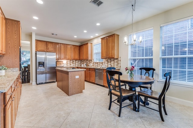 5801 Maidstone Dr, Richardson, TX 75082 - kitchen featuring appliances with stainless steel finishes, a kitchen island, decorative backsplash, a chandelier, and brown cabinets
