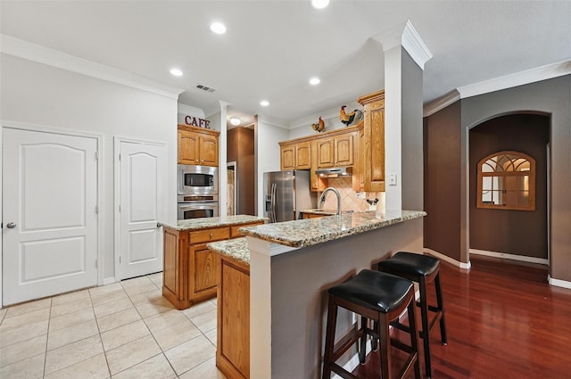 7917 Chapelwood Dr, North Richland Hills, TX 76182 - kitchen with appliances with stainless steel finishes, crown molding, a peninsula, arched walkways, and under cabinet range hood