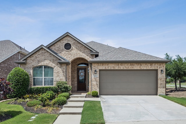 1117 Summer Ln, Mckinney, TX 75071 - french country home with brick siding, concrete driveway, an attached garage, and roof with shingles