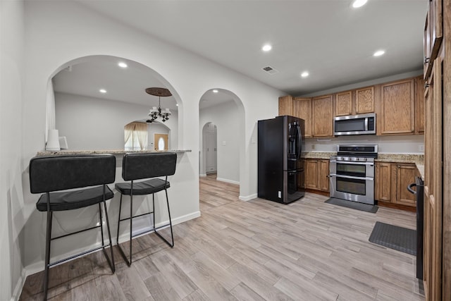 3208 Travis Ave, Fort Worth, TX 76110 - kitchen featuring appliances with stainless steel finishes, brown cabinets, arched walkways, recessed lighting, and light wood-style floors