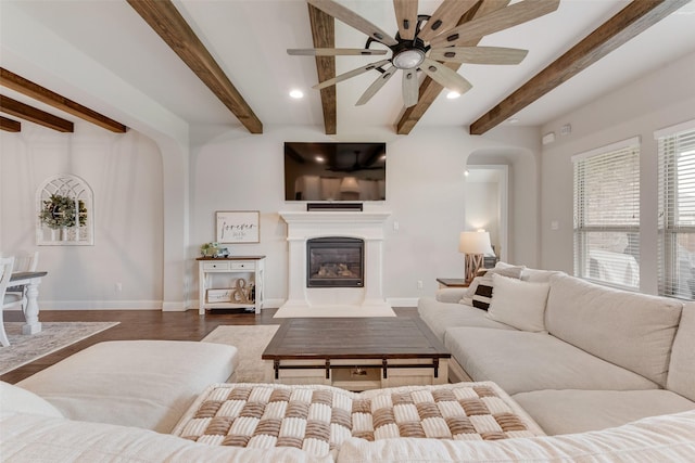 10321 Colina Dr, Fort Worth, TX 76126 - living area with arched walkways, a glass covered fireplace, beam ceiling, a ceiling fan, and dark wood-type flooring