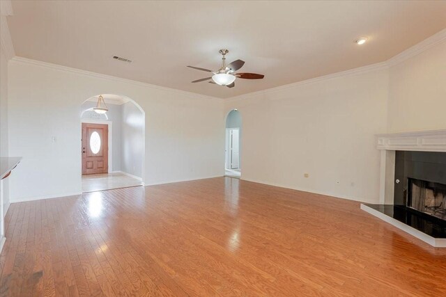 316 Cottonwood Trl, Shady Shores, TX 76208 - unfurnished living room featuring arched walkways, ceiling fan, wood finished floors, a tiled fireplace, and crown molding