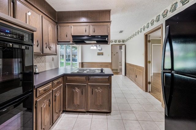 4508 Ramsgate Ct, Arlington, TX 76013 - kitchen featuring black appliances, under cabinet range hood, a textured ceiling, dark countertops, and a wainscoted wall