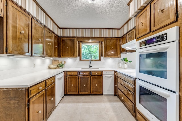 23 Crosslands Rd, Benbrook, TX 76132 - kitchen featuring white appliances, a textured ceiling, brown cabinetry, under cabinet range hood, and a sink