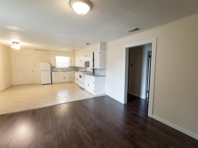921 Longino St, Sulphur Springs, TX 75482 - kitchen featuring white appliances, light wood finished floors, a textured ceiling, white cabinetry, and backsplash