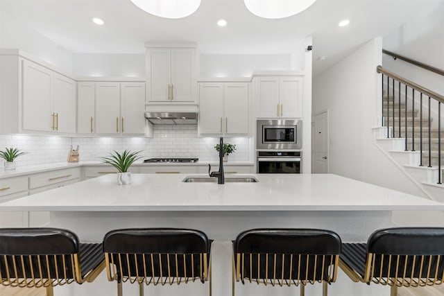 8509 Barnbougle Dunes Dr, Mckinney, TX 75070 - kitchen featuring appliances with stainless steel finishes, under cabinet range hood, a sink, a kitchen breakfast bar, and white cabinetry